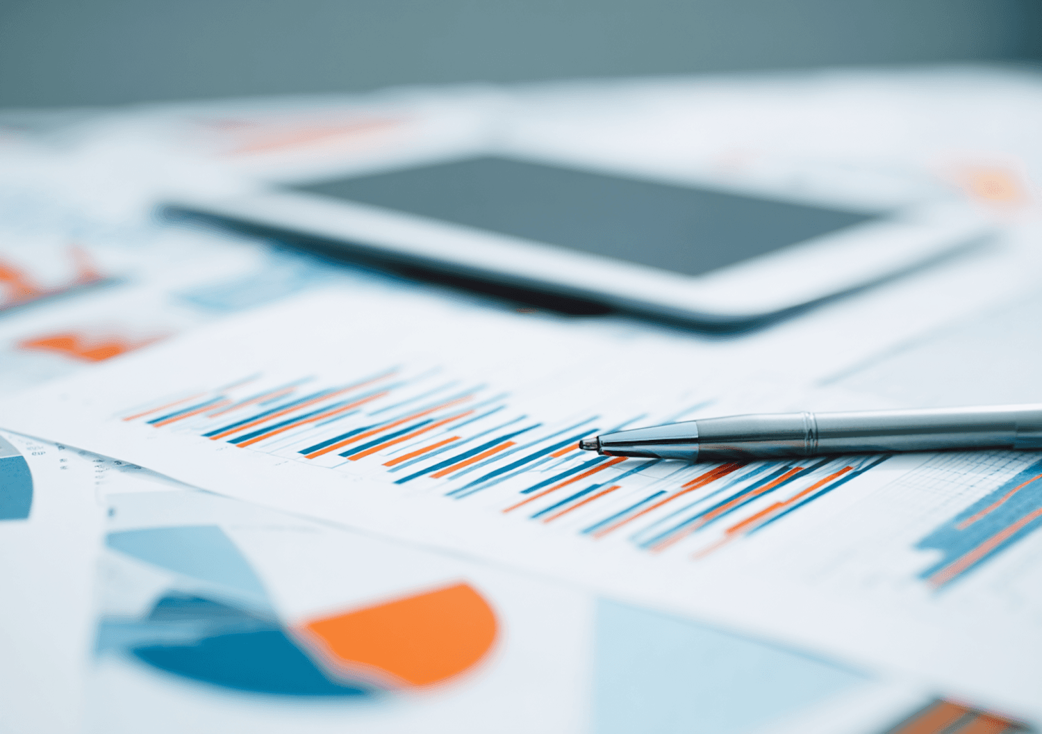Grafikë financiare, laps dhe tablet mbi një tavolinë pune